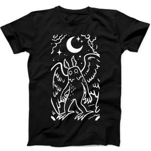 Może przedstawiać: Czarny t-shirt z krótkim rękawem z białym nadrukiem graficznym przedstawiającym skrzydlate stworzenie stojące pod półksiężycem i gwiazdami. Wzór jest zamknięty w prostokątnej ramce ze stylizowanymi chmurami i liniami, tworząc ilustrację o wysokim kontraście.