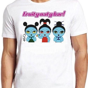 May include: A white short-sleeved t-shirt featuring a graphic print of three blue-skinned cartoon characters with distinct hairstyles. Above them, the text reads Fruity oaty bar! in pink, with Japanese characters to the left of the figures.