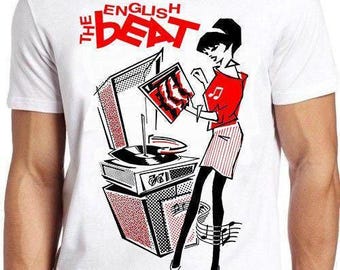 Puede incluir: Una camiseta blanca de manga corta con un estampado gráfico de un tocadiscos y una figura estilizada. El texto "THE ENGLISH BEAT" aparece en rojo sobre la ilustración, que utiliza los colores negro, blanco y rojo en su diseño.