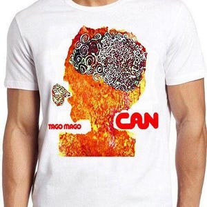 Può includere: Una t-shirt bianca a maniche corte con una stampa grafica di una testa stilizzata nei toniizzata nei toni dell'arancione, rosso e giallo. Il design include un motivo simile a un cervello con spirali nere e il testo Tago Mago e CAN in rosso.