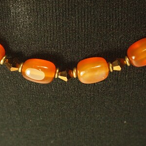 May include: A close-up of a necklace with orange carnelian beads and gold-toned spacers.