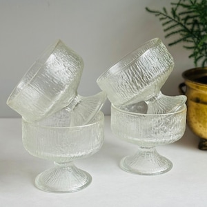 May include: Four clear glass dessert bowls with a textured surface and a pedestal base. The bowls are stacked on top of each other.