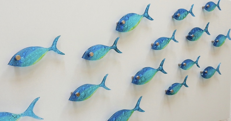 Pu&ograve; includere: Un'opera d'arte da parete con uno scuola di pesci di vetro blu e verde. I pesci sono disposti in uno schema fluido, creando un senso di movimento.