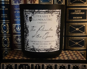May include: A matte black candle jar with a white rectangular label featuring a black ornate border and the text Literarily Illuminating Candles, The Phantom of the Opera, and I am not really wicked. Love me and you shall see! - Gaston Leroux.