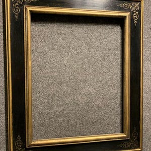 May include: A rectangular picture frame with a black exterior and gold interior. The frame has ornate gold corner detailing. The frame is empty, ready to display a photograph or artwork.