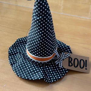 May include: A black and white polka dot witch hat with an orange and white ribbon. The hat has a brown tag that says "BOO!"