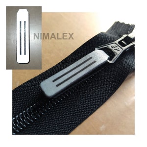 Pode incluir: Um close-up de um zíper preto com um puxador de zíper prateado. O puxador tem três linhas paralelas. O texto "NIMALEX" é visível no fundo.