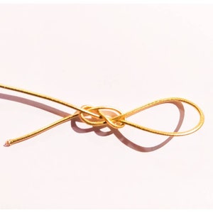 May include: A gold wire is tied in a knot, creating a loop. The wire is thin and shiny, and the knot is simple and elegant.