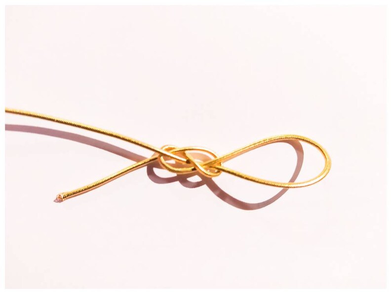 May include: A gold wire is tied in a knot, creating a loop. The wire is thin and shiny, and the knot is simple and elegant.