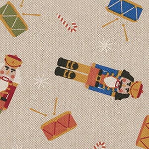 Op de afbeelding: Een beige stof met een herhalend patroon van notenkrakers, trommels en snoepstokken. De notenkrakers zijn in rood, blauw en goud. De trommels zijn in rood, blauw en goud. De snoepstokken zijn in rood en wit.