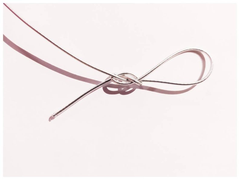 May include: A silver cord tied in a knot on a white background.
