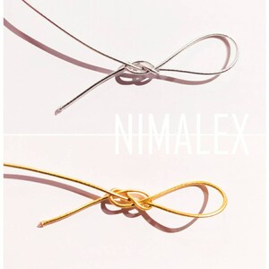 May include: Two pieces of wire, one silver and one gold, are tied in a knot. The wires are on a pink background.
