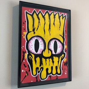 May include: A framed illustration of a yellow cartoon character with black hair, pink eyes, and a dripping yellow face on a red background with black and white splatters.