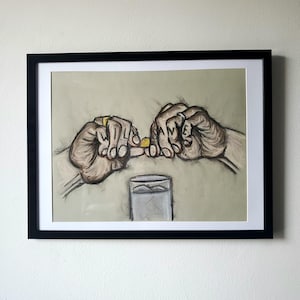 May include: A black and white drawing of two hands holding a small yellow pill. The hands are drawn with detail and the pill is in focus. The drawing is framed in a black frame and is hanging on a white wall.