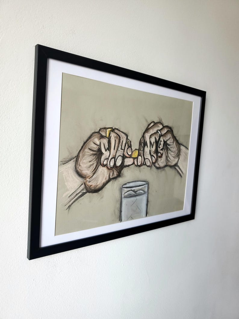 May include: A framed drawing of two hands holding a small yellow object, with the word "SAME" spelled out on the fingers of one hand. A glass of water is in the background.