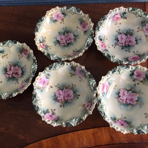 May include: Set of five antique porcelain bowls with a scalloped edge and floral design. The bowls are decorated with pink roses and green leaves on a cream background.