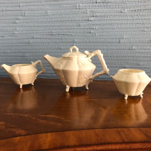May include: A white porcelain tea set with a teapot, creamer, and sugar bowl. The set features a delicate floral design and intricate details.