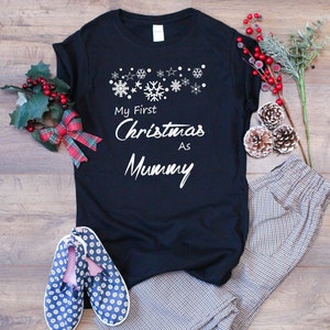 May include: Black t-shirt with white text that reads "My First Christmas As Mummy" and a row of white snowflakes and stars above the text.