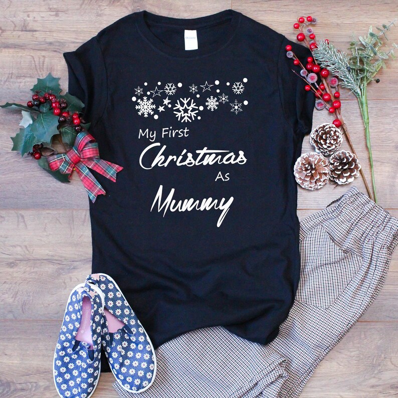 May include: Black t-shirt with white text that reads "My First Christmas As Mummy" and a row of white snowflakes and stars above the text.