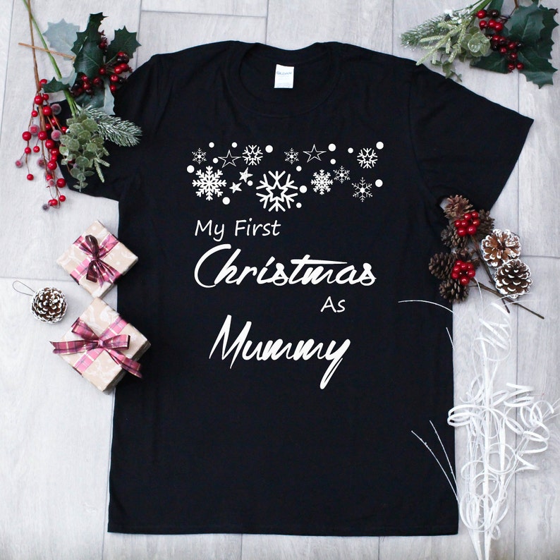 May include: Black t-shirt with white text that reads "My First Christmas As Mummy" with a row of snowflakes and stars above the text.