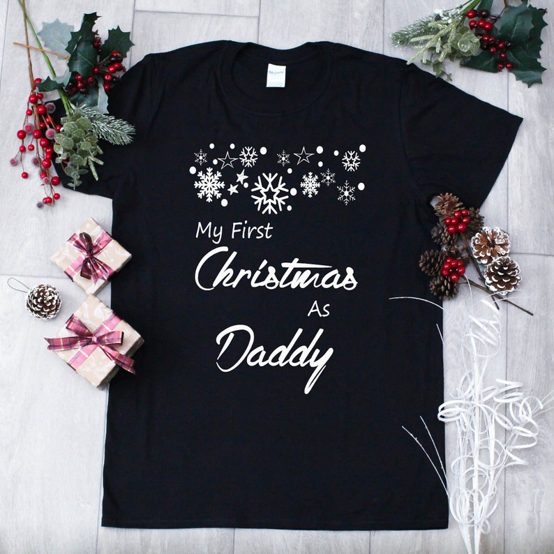 May include: Black t-shirt with white snowflakes and the text "My First Christmas As Daddy".