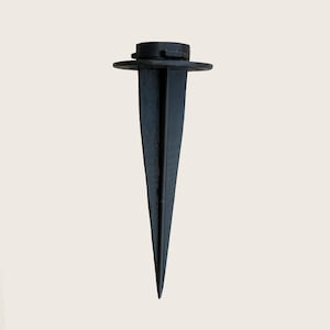 May include: A black landscape stake with a flat top and a pointed bottom. The stake is designed to hold landscape lighting or other outdoor fixtures. The stake is made of a durable material and is suitable for various outdoor applications.