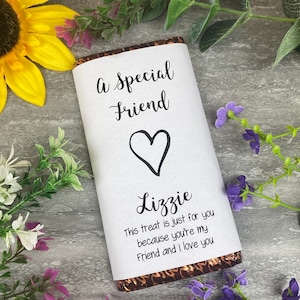 Może przedstawiać: Biały papierowy owijak na tabliczkę czekolady z tekstem "A Special Friend" i sercem. Owijak zawiera również imię "Lizzie" i wiadomość "This treat is just for you because you're my Friend and I love you".
