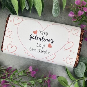 Op de afbeelding: Een witte chocoladeverpakking met een roze hartontwerp en de tekst "Happy Galentine's Day! love Cheryl x".