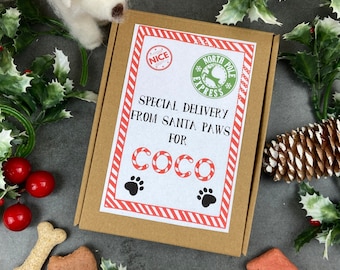 May include: A brown box with a red and white striped border. The box has a white label with the text "Special Delivery from Santa Paws for Coco" and a red and white candy cane design. The box is surrounded by green holly and red berries.