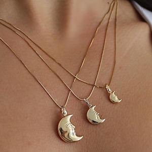 Puede incluir: Tres collares de tono dorado con colgantes de media luna que presentan un diseño de rostro humano. Cada collar tiene una cadena delicada de diferentes longitudes, lo que permite que los tres dijes de luna cuelguen a distintos niveles.