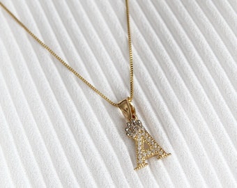 Op de afbeelding: Een gouden ketting met een hanger in de vorm van de letter A. De hanger is bezet met kleine, heldere stenen.
