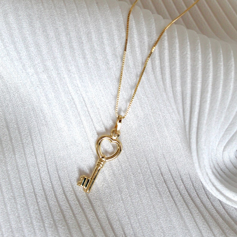 Peut inclure: Un collier en or avec un pendentif en forme de cl&eacute; de c&oelig;ur. Le collier est sur un fond blanc.