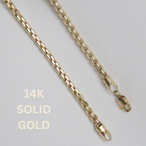 May include: Two gold necklaces with a box chain design are displayed against a white background. The text "14K SOLID GOLD" is printed in white. The necklaces are connected with a lobster clasp.