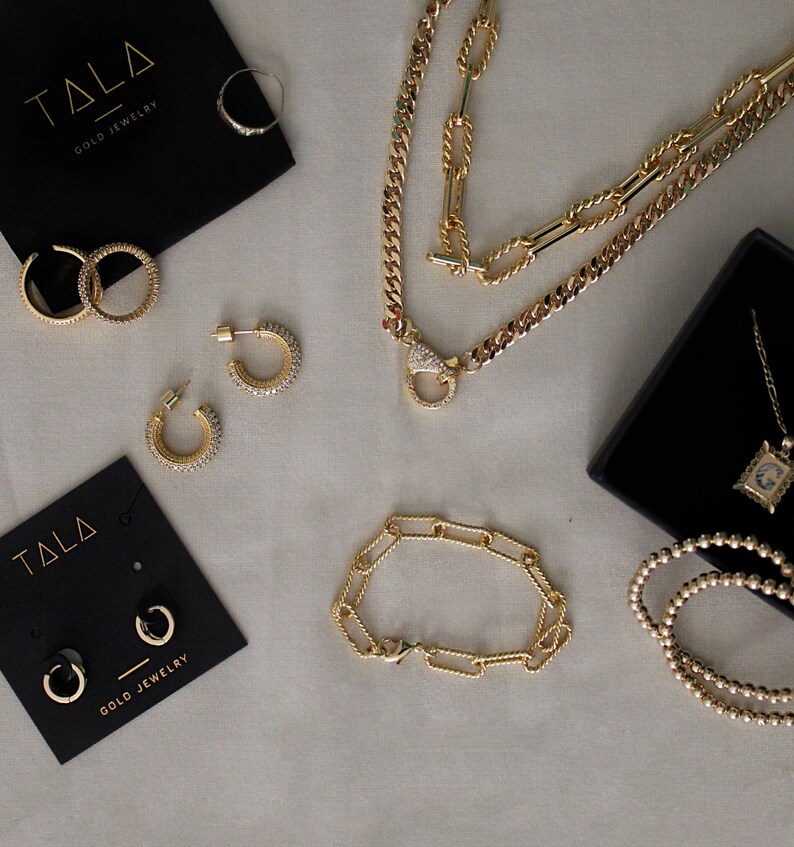 Peut inclure: Une collection de bijoux en or pr&eacute;sentant une vari&eacute;t&eacute; de styles, notamment des colliers, des bracelets, des boucles d'oreilles et des bagues. Les bijoux sont pr&eacute;sent&eacute;s sur une surface blanche avec des bo&icirc;tes noires.