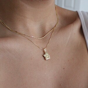 May include: Two gold necklaces layered on a person's chest. The bottom necklace has a small angel pendant.