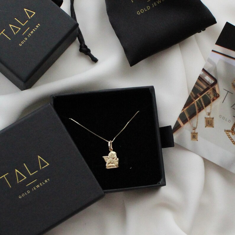 May include: A gold angel pendant necklace in a black jewelry box with the brand name "Tala Gold Jewelry" on the box.