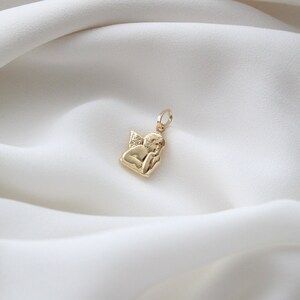 May include: A gold-toned pendant charm featuring a cherub angel with wings, holding its chin in thought.