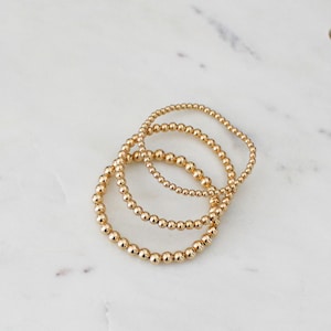 Peut inclure: Trois bracelets en perles dorées empilés les uns sur les autres. Les bracelets sont faits de petites perles rondes.