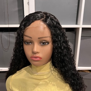 May include: A black curly human hair wig on a mannequin head with a yellow turtleneck top. The wig is long and has a lace front.