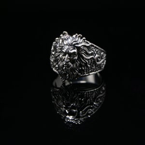 Peut inclure: Une bague en argent avec un design détaillé d'un visage d'homme avec une barbe et des cheveux longs. La bague est sur un fond noir.