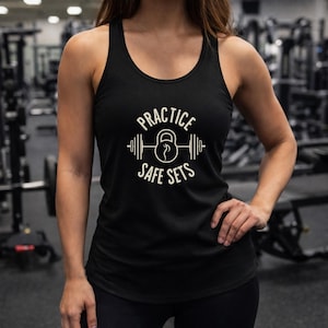May include: Black racerback tank top with the text "PRACTICE SAFE SETS" in white. The design includes a barbell and kettlebell graphic. The tank top is worn in a gym setting.