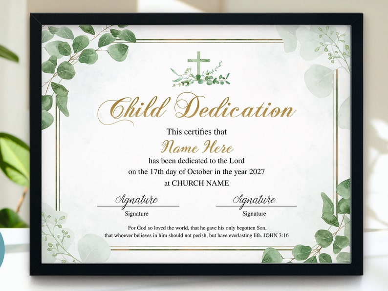 May include: A framed Child Dedication certificate with a black frame. The certificate has gold text and a cross design. Green eucalyptus leaves and branches decorate the corners and edges. The text includes "Name Here" and "CHURCH NAME".