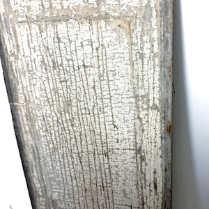 May include: A rectangular wooden board featuring a heavily distressed, cracked white paint finish. The surface displays a visible network of fine fissures and weathered texture, with natural wood tones showing through the worn areas along the edges.