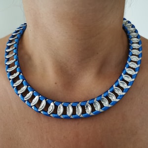 Op de afbeelding: Een opvallende blauw-zilveren ketting. De ketting heeft een levendig blauw geweven koordontwerp, afgewisseld met zilverkleurige, ovaalvormige metalen elementen. Dit opvallende sieraad is perfect om een vleugje kleur en textuur aan elke outfit toe te voegen.