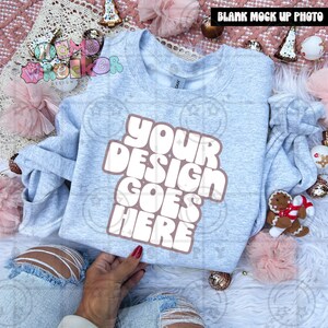 May include: A light gray sweatshirt with the text "YOUR DESIGN GOES HERE" in a brown font. The sweatshirt is surrounded by holiday decorations, including ornaments and a gingerbread man.