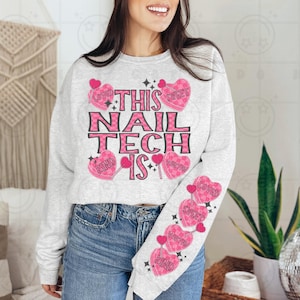 Puede incluir: Una sudadera gris con el texto "This Nail Tech Is" en letras negras. La sudadera tiene corazones de caramelo rosa con diferentes palabras en ellos, como "Loved", "Sweet", "Worth" y "Kind".