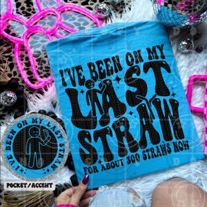 Puede incluir: Una camiseta azul claro con el texto "I'VE BEEN ON MY LAST STRAW FOR ABOUT 300 STRAWS NOW" en negro. El diseño retro incluye una figura de palo con una pajita. También se ve un adorno a juego.