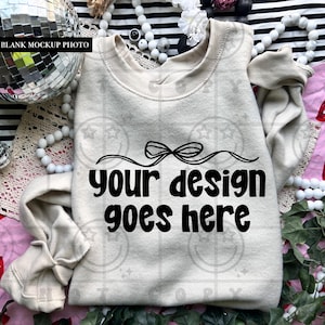 Puede incluir: Una sudadera de color crema con el texto "your design goes here" en negro y en negrita. La sudadera es una maqueta en blanco, perfecta para mostrar diseños personalizados. La imagen incluye elementos decorativos.
