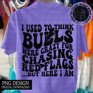 May include: A light purple t-shirt with the text "I USED TO THINK BULLS WERE CRAZY FOR CHASING RED FLAGS...BUT HERE I AM" in black. The shirt also has a graphic of a bull. The words "PNG DESIGN DIGITAL DOWNLOAD" are at the bottom.