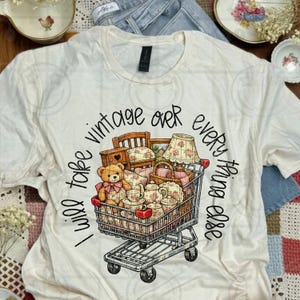 May include: Cream-colored t-shirt with the phrase "I will take vintage over everything else" in black script. A shopping cart graphic is filled with vintage items, including a teddy bear, furniture, and teacups.